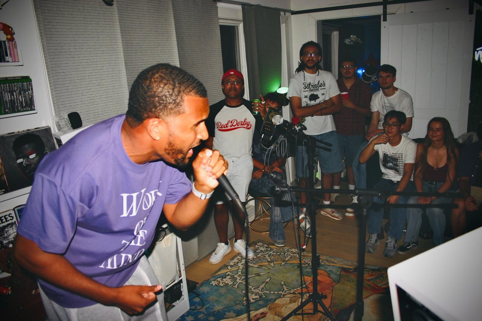 A performer in a purple t-shirt sings into a microphone while the audience watches.