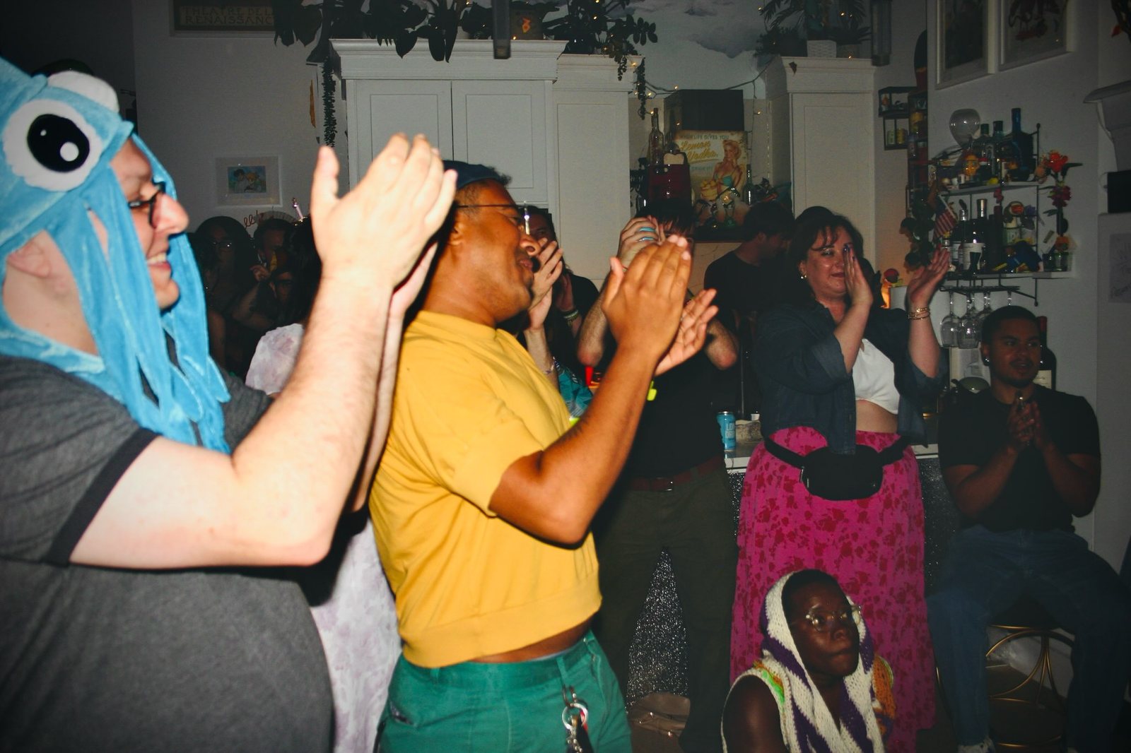 Audience members, one in a blue costume hood, clap and cheer.