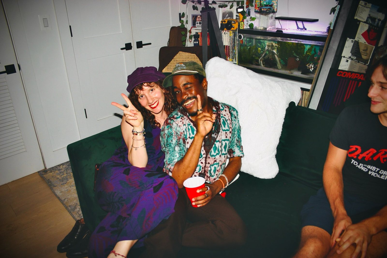 Guests laughing on a couch, one holding a red cup.