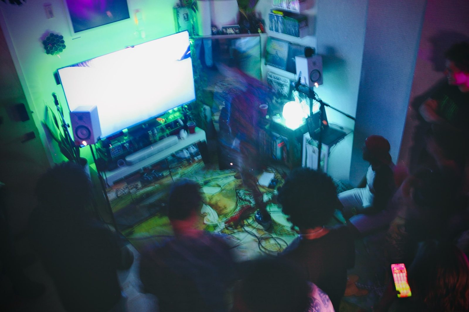 A dark room lit green and purple, with a glowing screen.